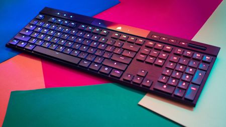 Sleek black keyboard with colorful backlighting on a vibrant background of red, blue, and green paper, conveying a modern and tech-savvy vibe.