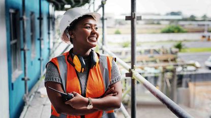 A black female construction worker smiles as she looks out at an ongoing project
