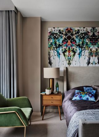 beige bedroom with statement artwork, green velvet chair and mid-century modern bedside table