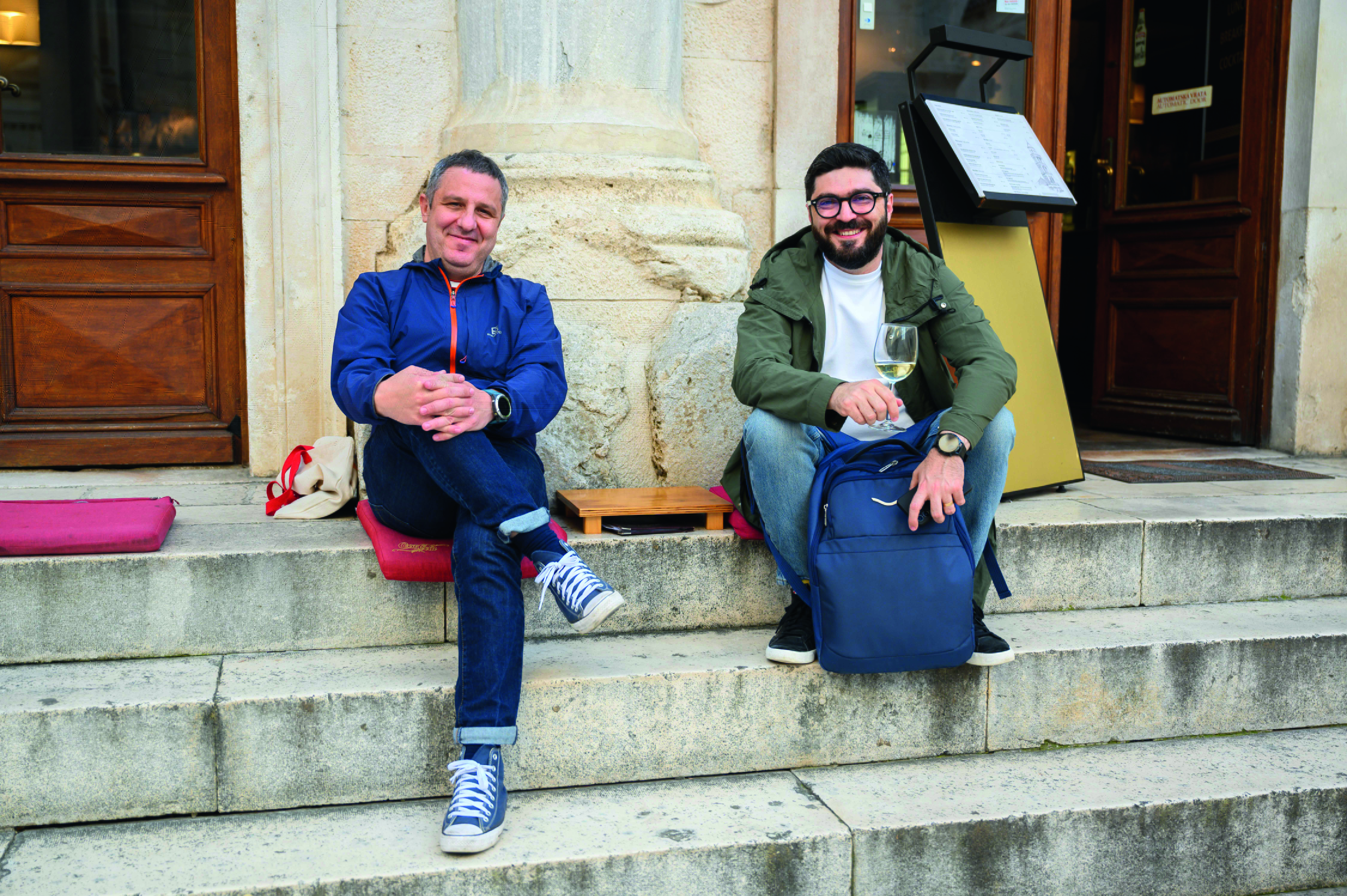 Two men sitting on steps, with a glass of white wine