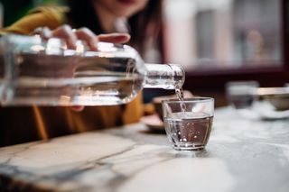 Woman pouring water into a glass from a bottle at a table