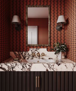 bathroom with retro orange and black wallpaper, marble topped vanity, chocolate brown panelled cabinetry, mirror, wall lights