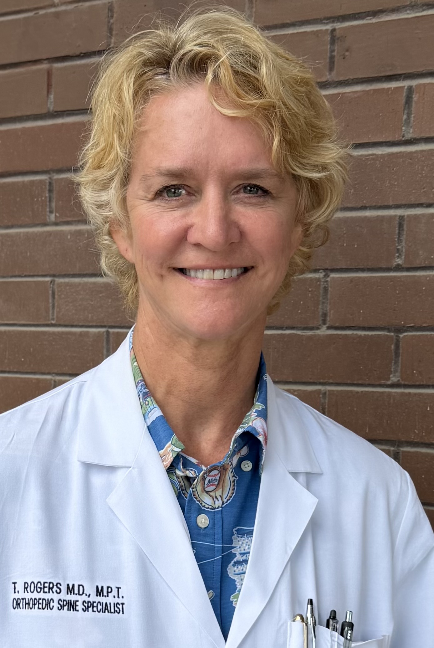 Head of shoulders of woman wearing white doctor's coat, with the following written on it: T. Rogers M.D., M.P.T. Orthopedic spine specialist