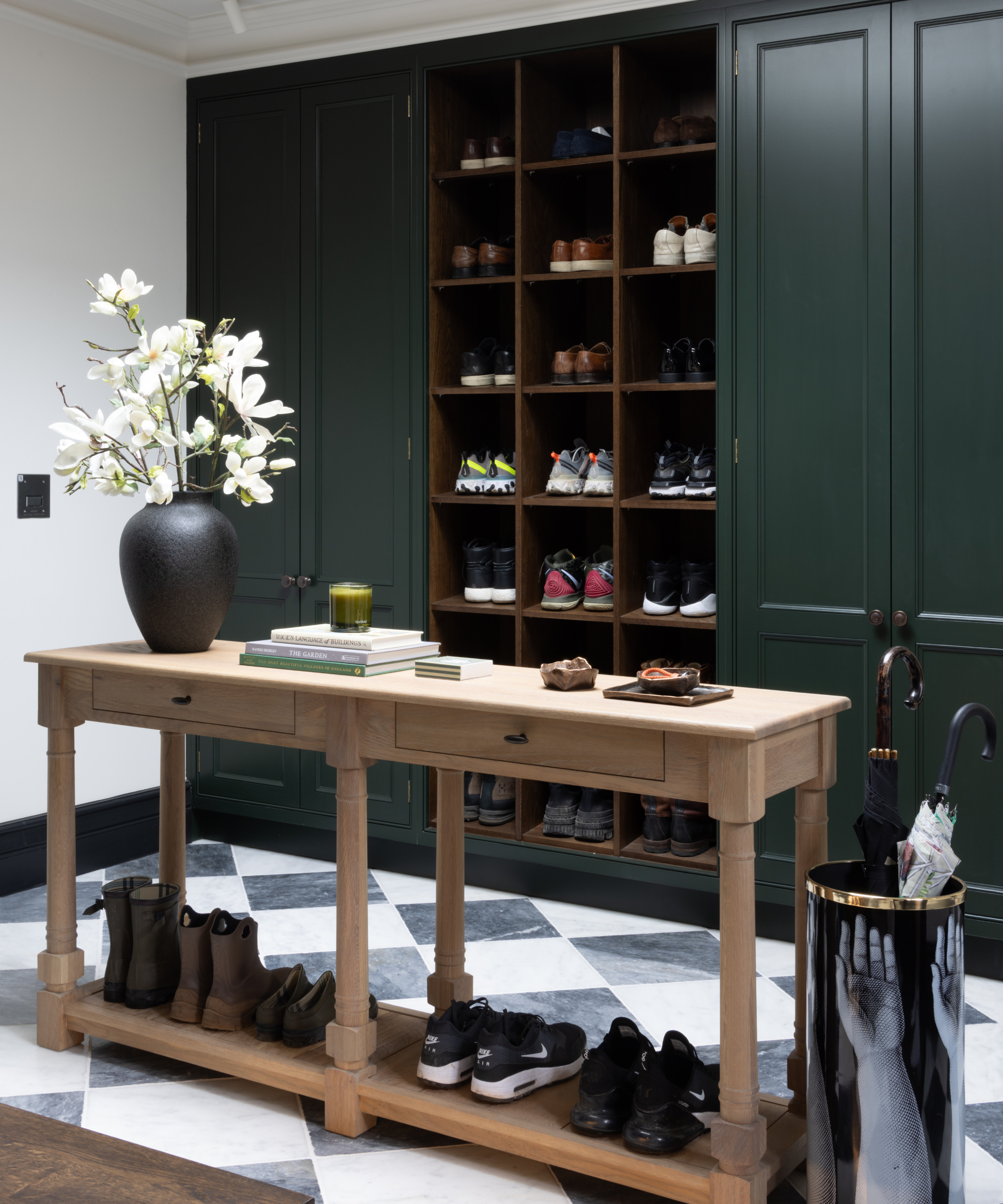 boot room with large green cabinet and shelving on one wall, narrow wooden console table in middle of rooms with lower shelf housing shoes