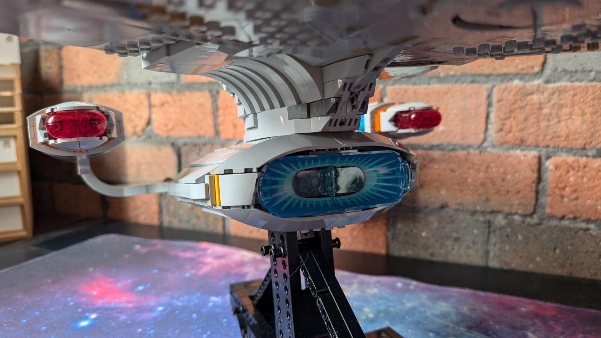 Lego U.S.S. Enterprise set on stand, with a brick wall visible in the background