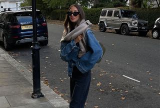 Woman wearing jeans with an oversize denim jacket and a gray sweater around her shoulders.