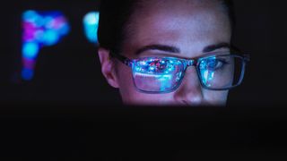Woman testing software, looking into a screen with lights reflecting in her glasses