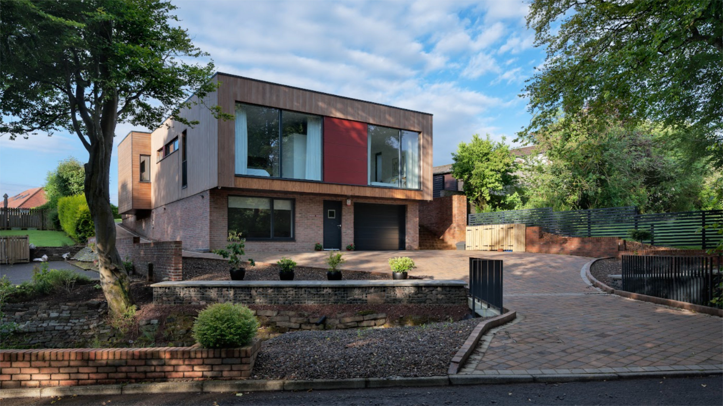 The exterior of a modern home with a large paved driveway and extensive glazing