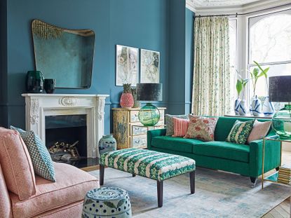 Living room with bright green sofa and assorted cushions, padded stool and sash window with light cushions and blue walls