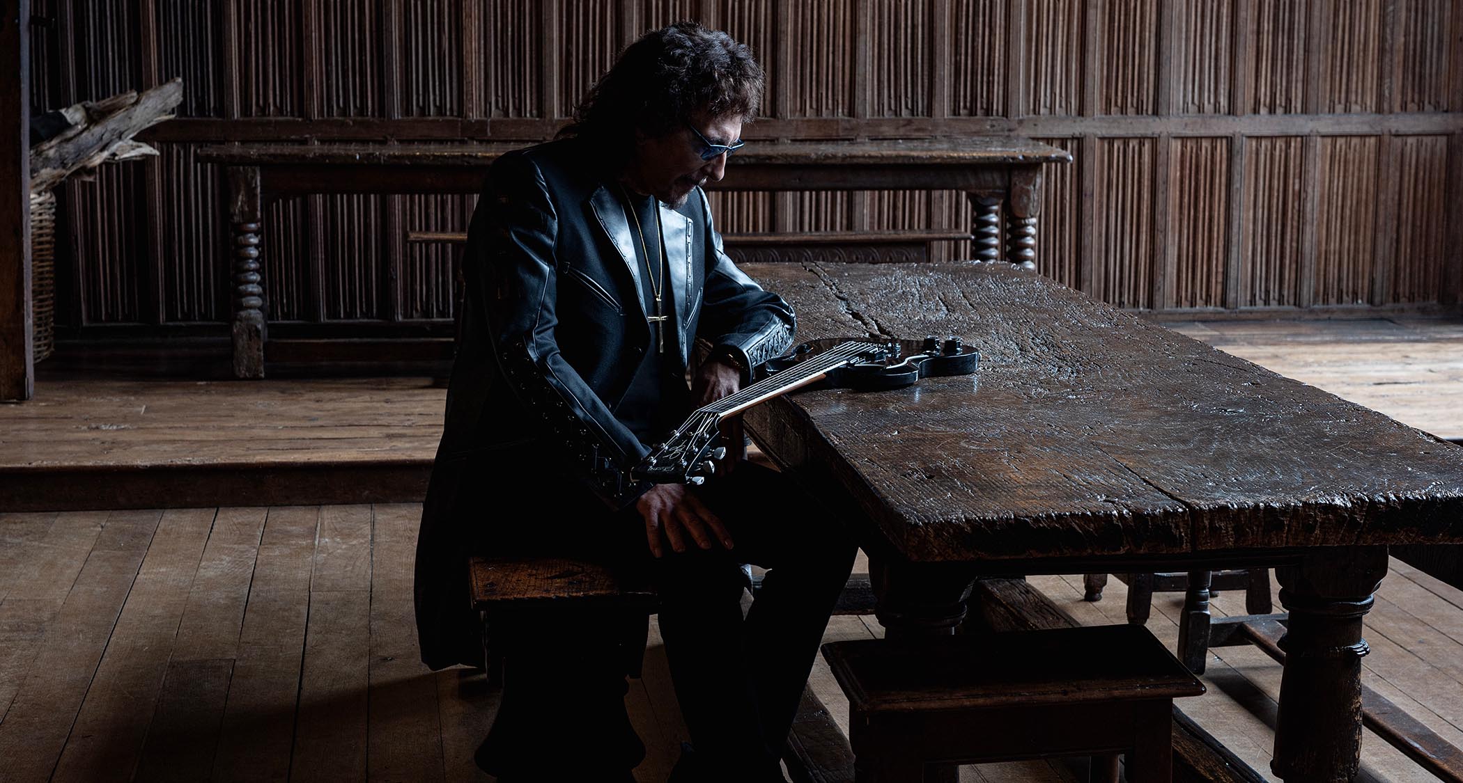 Tony Iommi sits at an old table and contemplates his guitar.