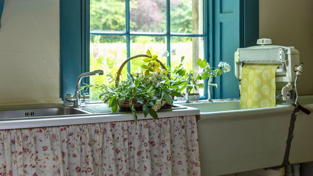 kitsch kitchen sink with floral white and red sink skirt and bright blue crittal window looking out over countryside