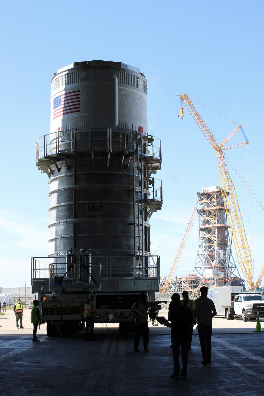 a large section of a rocket stands in a factory entryway, blue sky shining behind it.