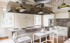 Mimo London cookery school teaching kitchen with marble benches with cutting boards and knives and a bench of cooking plates