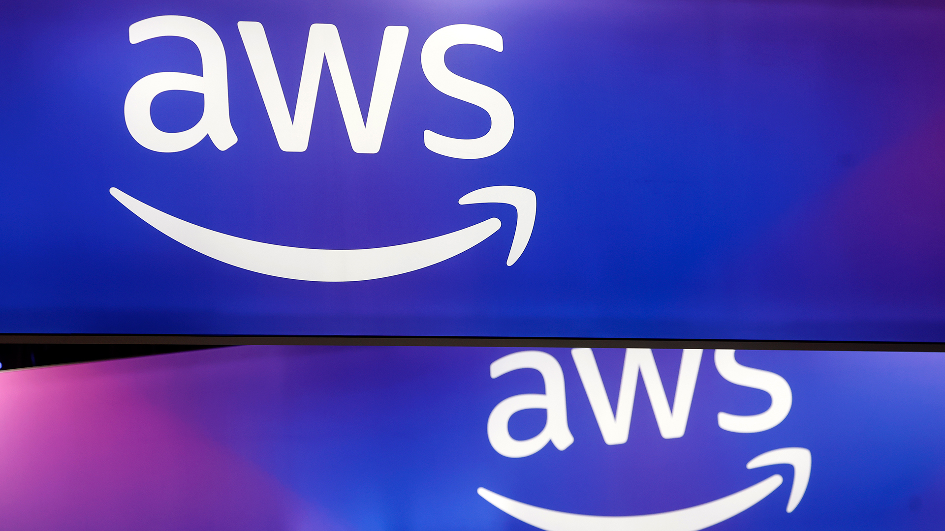 A telephoto shot of the AWS logo on two intersecting screens, against a blue and purple gradient background.