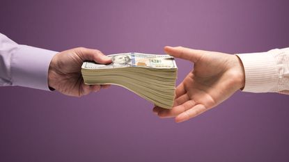 A man hands a woman a thick stack of cash, only their hands showing.