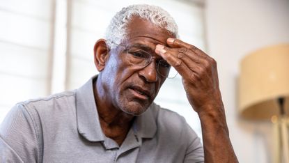 An older man looks down, looking stressed.