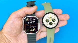 Close-up of the Apple Watch Ultra 3 and Google Pixel Watch 5 in a user's hand against a bright blue background
