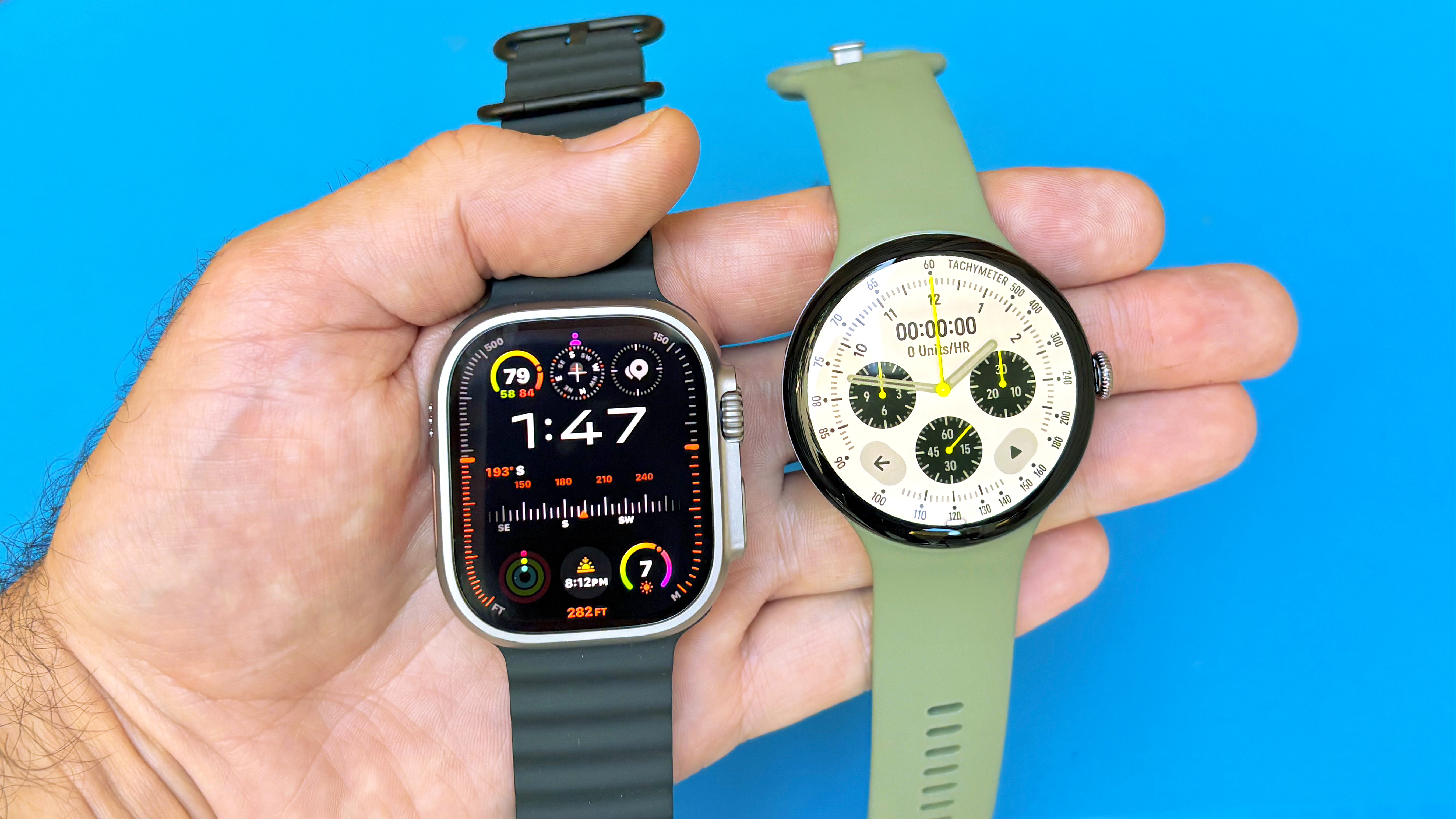Close-up of the Apple Watch Ultra 3 and Google Pixel Watch 5 in a user's hand against a bright blue background