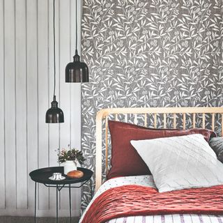 A bedroom with a wall covered in botanical wallpaper and a bed with white and burgundy bedding