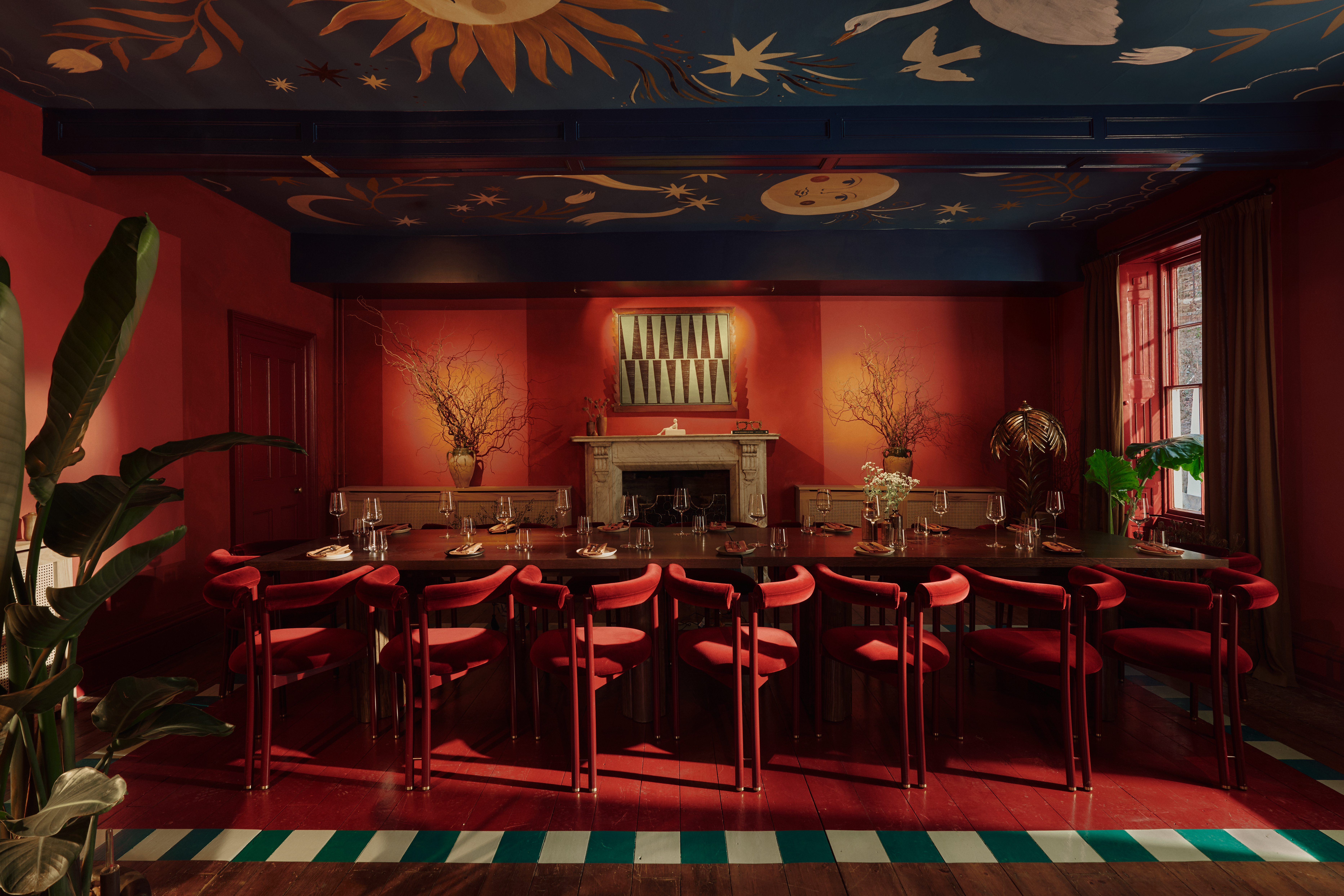 The interior of a private members' club's bar and lounge, decorated with sprawling wall and ceiling murals, earthy tones, plush furniture, and plenty of artworks.