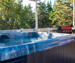 A large aqua blue colored empty hot tub on a patio deck next to a red BBQ