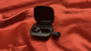 The Beats Fit Pro true wireless earbuds against a silky red surface.