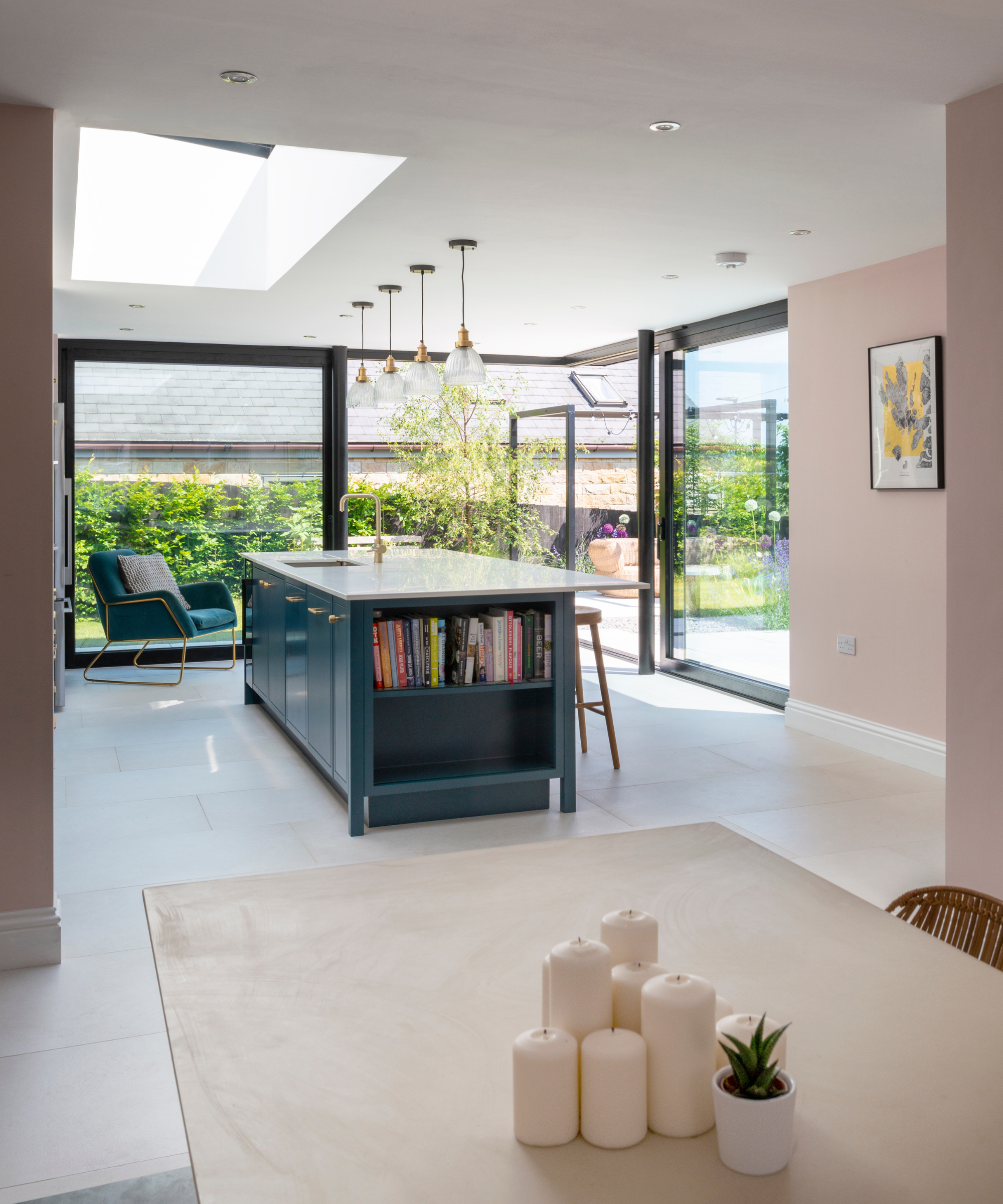Kitchen with glass patio doors wrapping round the right corner, a blue kitchen island with book storage, and a white table with candles and a plant