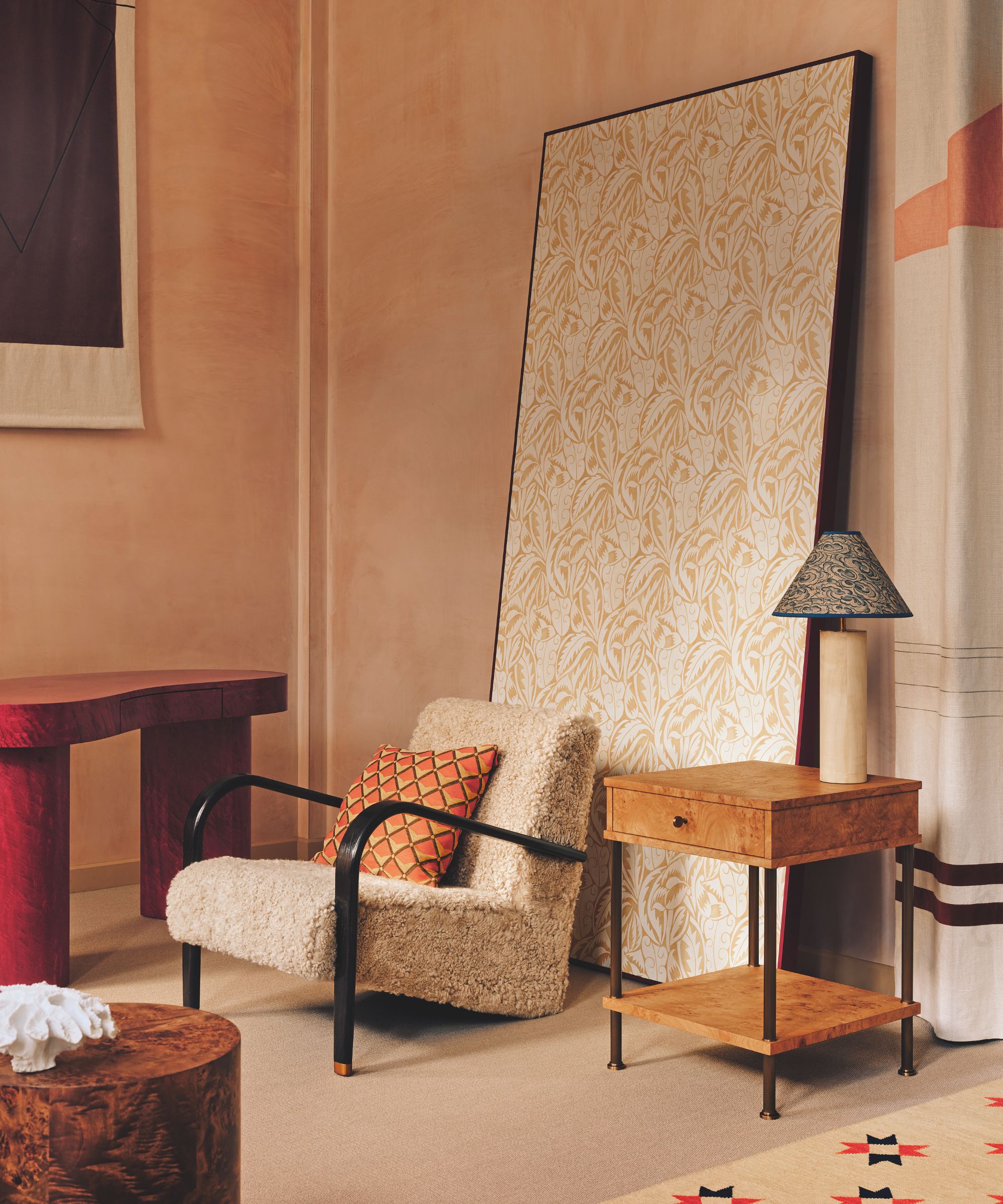 A cozy corner featuring a cream-colored sherpa armchair with black frame arms, a burl wood side table, and a large leaning screen with a delicate cream-and-gold floral pattern.