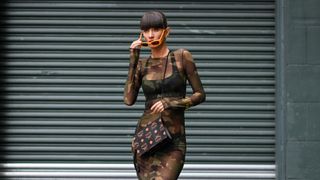 Katya Tolstova is seen wearing a Heron Preston khaki camouflage maxi sheer dress, Versace bralette, MCM wristlet zip pouch, Moschino mustard yellow sunglasses and Movado gold bracelet on August 01, 2023 in New York City.