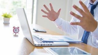 A man raising his hands up in frustration while looking at his laptop