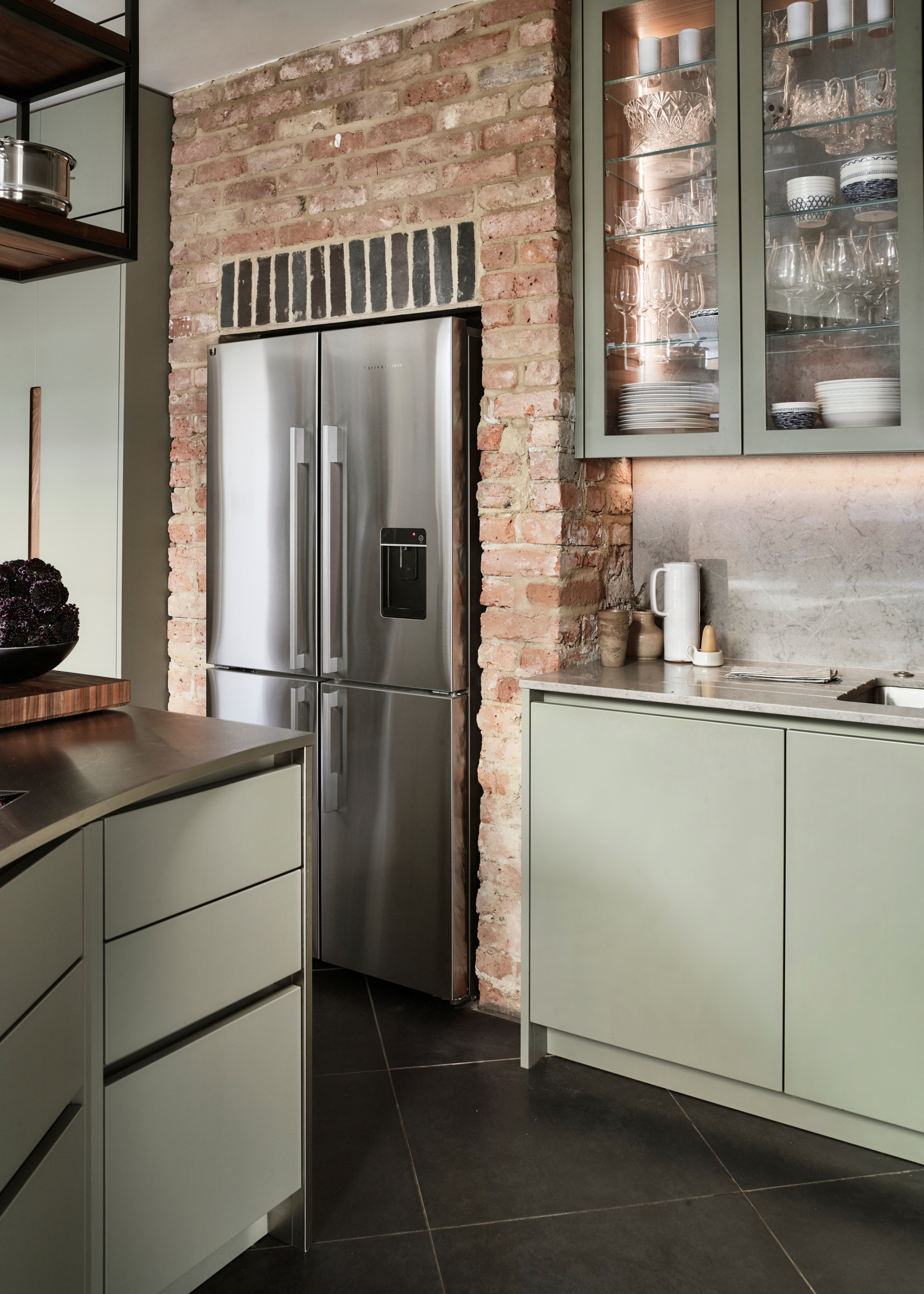 kitchen with exposed brick walls, sage green cabinetry, and stainless steel counters
