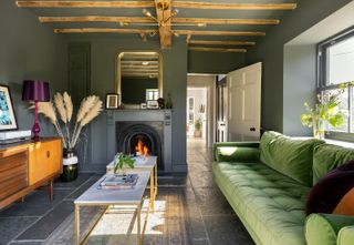 cosy living room in farmhouse with flagstone floors and open fire and green sofa