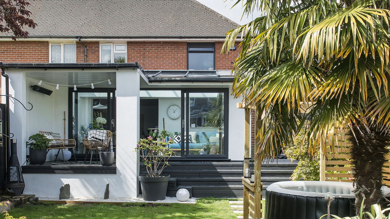 Garden with large lawn area and hot tub leading to white rendered rear extension with decking