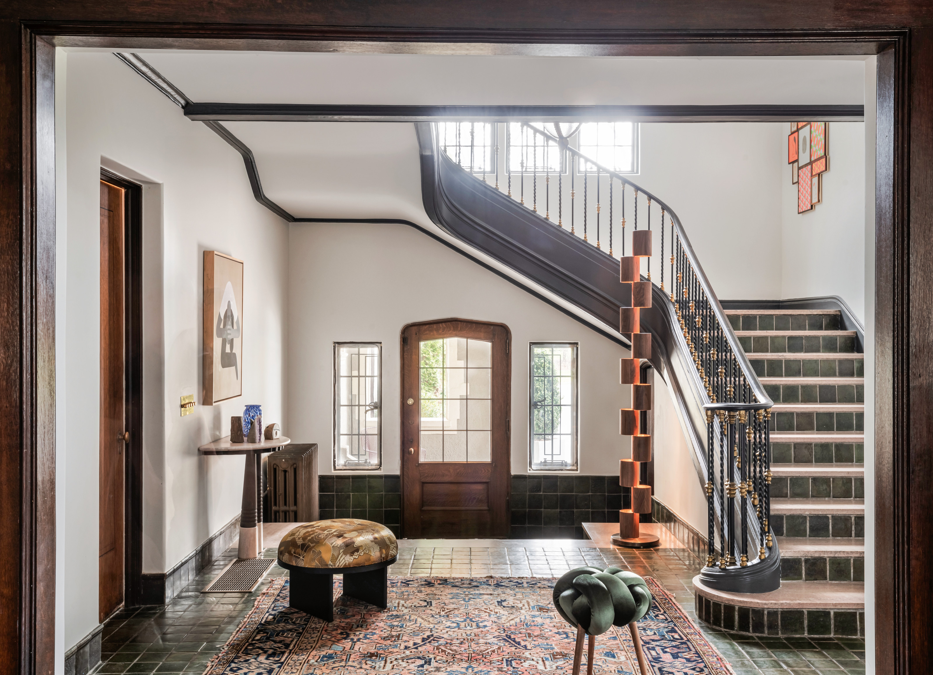 Grand hallway with tiled sweeping staircase, green tiled floor, white walls and totem-style floor lamp