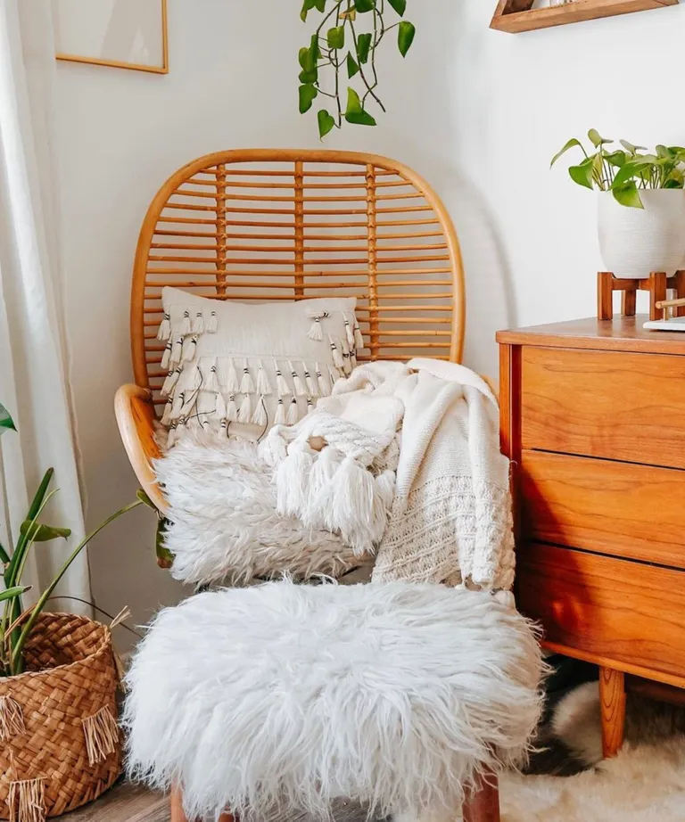 A woven chair with a white cushion and throws, plus plants around it