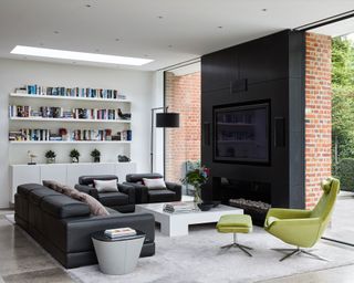 Sitting room with black leather furniture sofa and armchairs, a green armchair, white coffee table and a black fire surround with glass walls either side