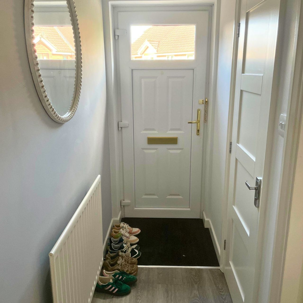 Grey narrow hallway with a mirror and a radiator on the wall, with shoes on the floor