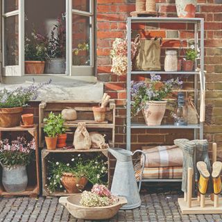 Potting station area on patio in garden with plant pots and wooden and metal shelving