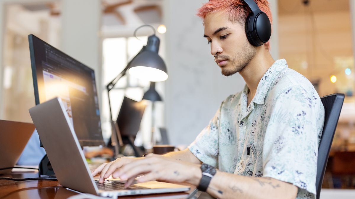 Male software developer sitting at desk coding in PHP programming language on a laptop device.