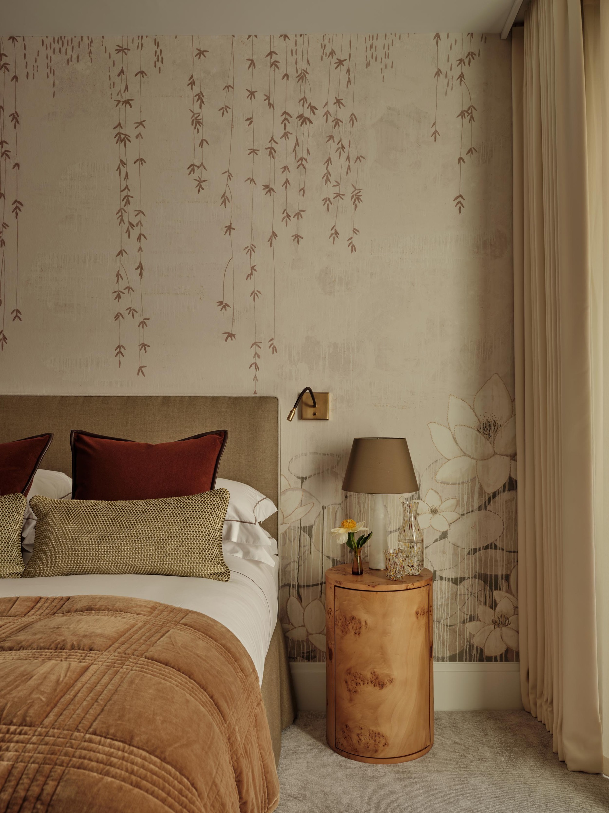 A bedroom with a neutral color palette, a curved burlwood nightstand, and a floral wallpaper