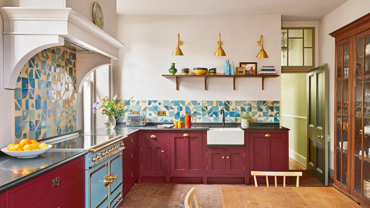 a kitchen with dark red cabinets with brass cup pulls, and a striking blue graphic tiled splashback and a large Belfast sink with black tap