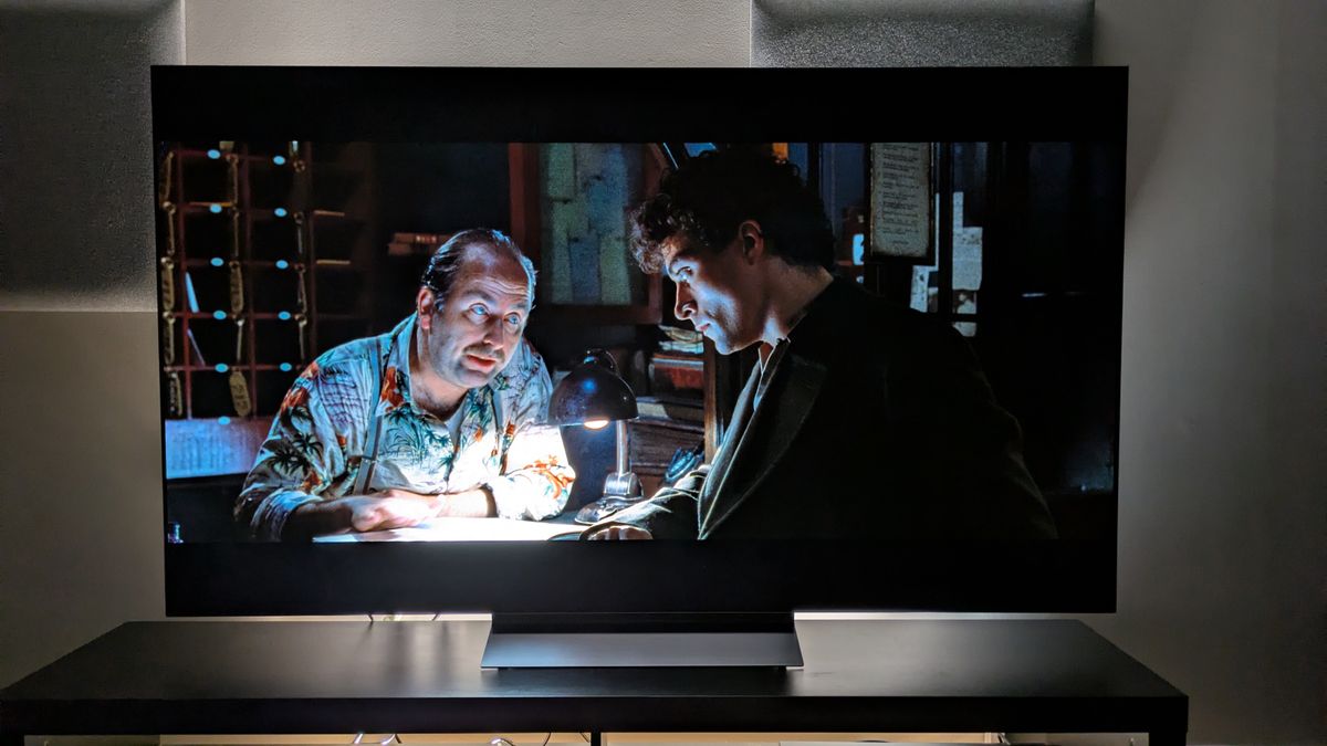 The LG C6 OLED TV with Dark City on screen, showing John chatting to a hotel clerk. The shot demonstrates the C6's powerful contrast, with strong shadows balancing with the bright desk light