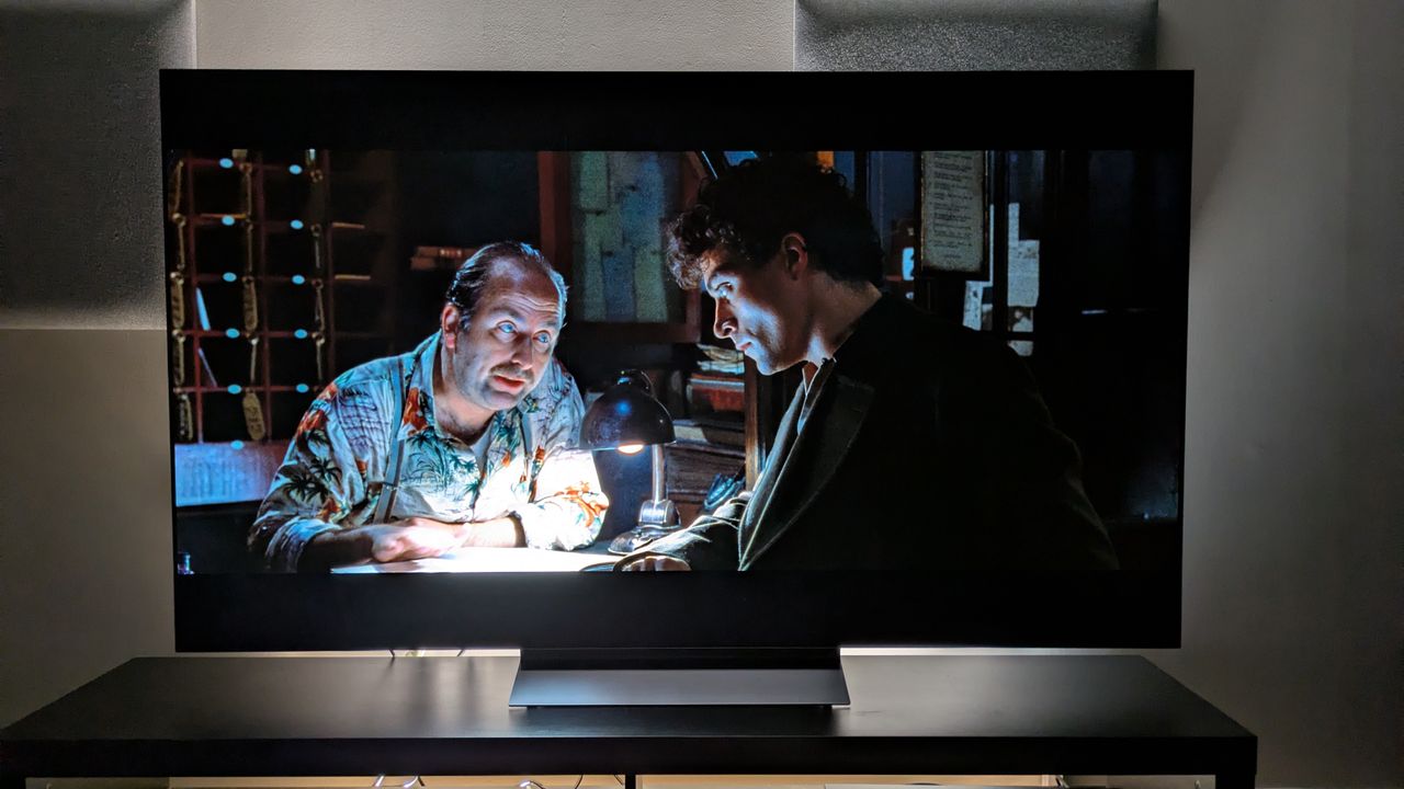 The LG C6 OLED TV with Dark City on screen, showing John chatting to a hotel clerk. The shot demonstrates the C6's powerful contrast, with strong shadows balancing with the bright desk light