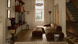beige living room with khaki sofa, parquetry floors, wall bracket with timber, beige curtains, rug, and timber side table with artwork above, and view of stairs