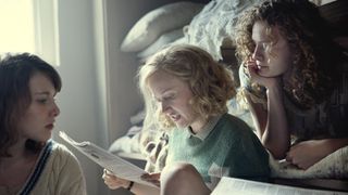 Zoe Brough as Jessica Mitford, Shannon Watson as Unity Mitford and Orla Hill as Debo Mitford sit together reading a paper Outrageous