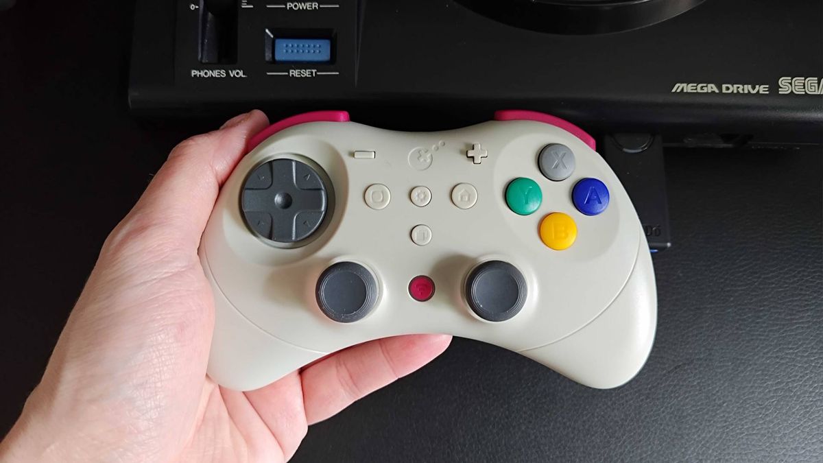Hand holding Gulikit Elves 2 Pro in front of Japanese Sega Mega Drive.