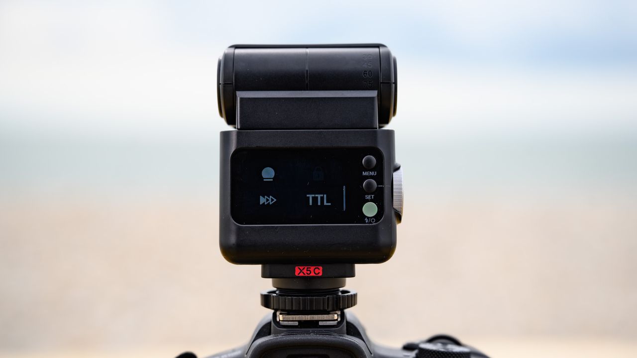 Closeup of the Godox iT32 camera flash and its rear display, the ocean is behind it