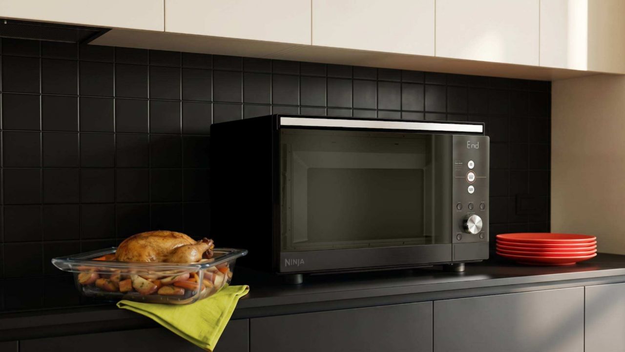 Ninja Crispi Microwave on a counter next to a roast chicken which has been cooked inside it