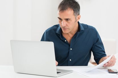 Portrait Of A Mature Man Looking At Laptop Holding Document