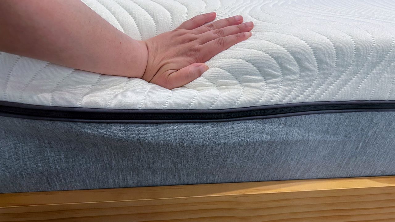 Hand pressing down on an edge of the Emma Comfort Mattress